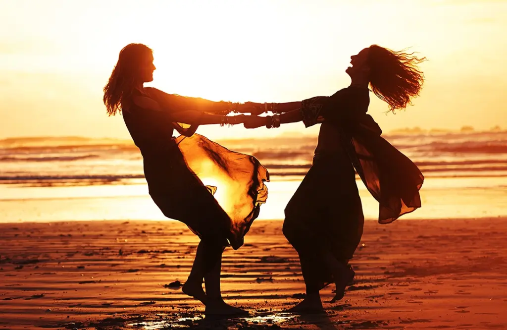 Zwei Frauen die, voller Lebensfreude, im Sonnenuntergang am Strand tanzen